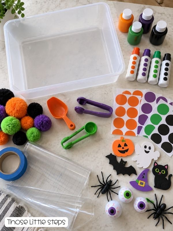 Toddler Halloween activity supplies, including washable paint, dot markers, stickers, pom-poms, painter’s tape, sensory tools, contact paper, and plastic decorations.